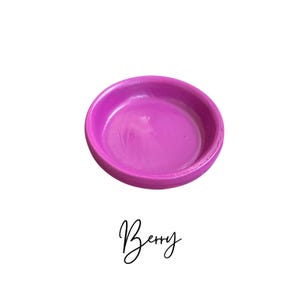 May include: A small, round, magenta-colored ceramic dish. The dish is empty and has a smooth, glossy finish.