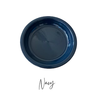 May include: A navy blue ceramic bowl with a glossy finish. The bowl is round with a slightly raised rim. The word "Navy" is written in cursive script below the bowl.