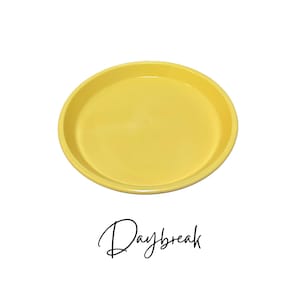 May include: A bright yellow ceramic saucer for a plant pot. The saucer is round and has a smooth, glossy finish.