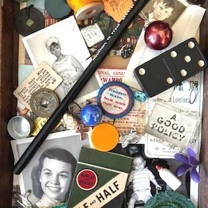 May include: A collection of vintage ephemera, including photographs, a domino, a pencil, and a cigarette pack. The items are arranged in a wooden box, with a spool of orange thread and a blue and white pin.