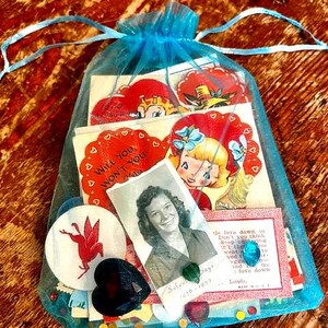 May include: A blue drawstring bag filled with vintage Valentine's Day cards, a black heart-shaped object, and a photo of a woman. The cards feature illustrations of children and the text "Will You Won't You".