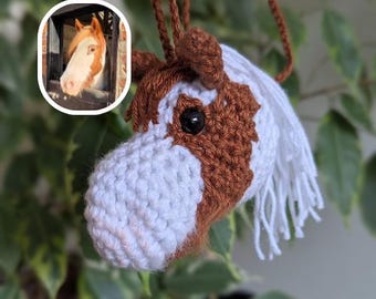 May include: A handmade crochet horse head ornament with brown and white details, including a white mane and a black eye. The horse head is suspended by a brown cord. A small inset image of a horse's head is in the upper left corner.