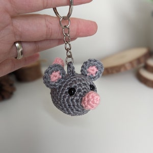 May include: A handmade crochet mouse keychain. The mouse is gray with pink accents on the ears and nose, and black eyes. The keychain is attached to a silver metal ring.