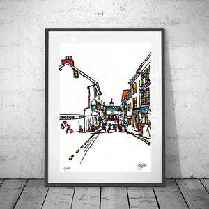 Puede incluir: Impresión artística enmarcada de una escena callejera con edificios y personas. La obra de arte presenta un contorno negro con acentos coloridos, incluyendo rojo, amarillo y azul. La impresión se muestra en un marco negro.