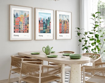 May include: Three framed prints of colorful cityscapes with the word "Phoog" printed below each image. The prints are hanging on a white wall above a wooden dining table with four chairs.