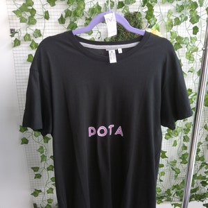 Può includere: Maglietta nera con una grafica rosa "DOTA" stampata sul davanti.