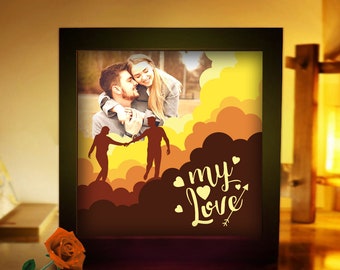 Puede incluir: Un marco de madera marrón con una imagen iluminada de una pareja frente a un fondo nublado amarillo y naranja. El texto "my love" está escrito en blanco con corazones y una flecha.