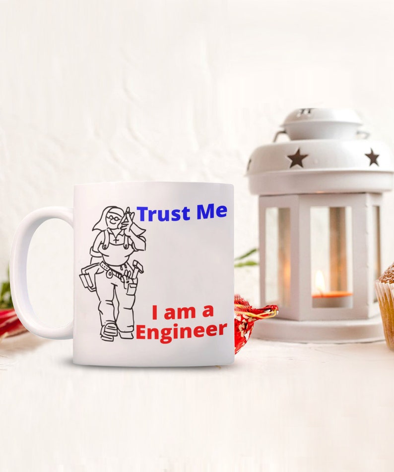 May include: White ceramic mug with a black line drawing of a woman wearing a tool belt and holding a wrench. The text "Trust Me I am a Engineer" is printed in blue and red on the mug.