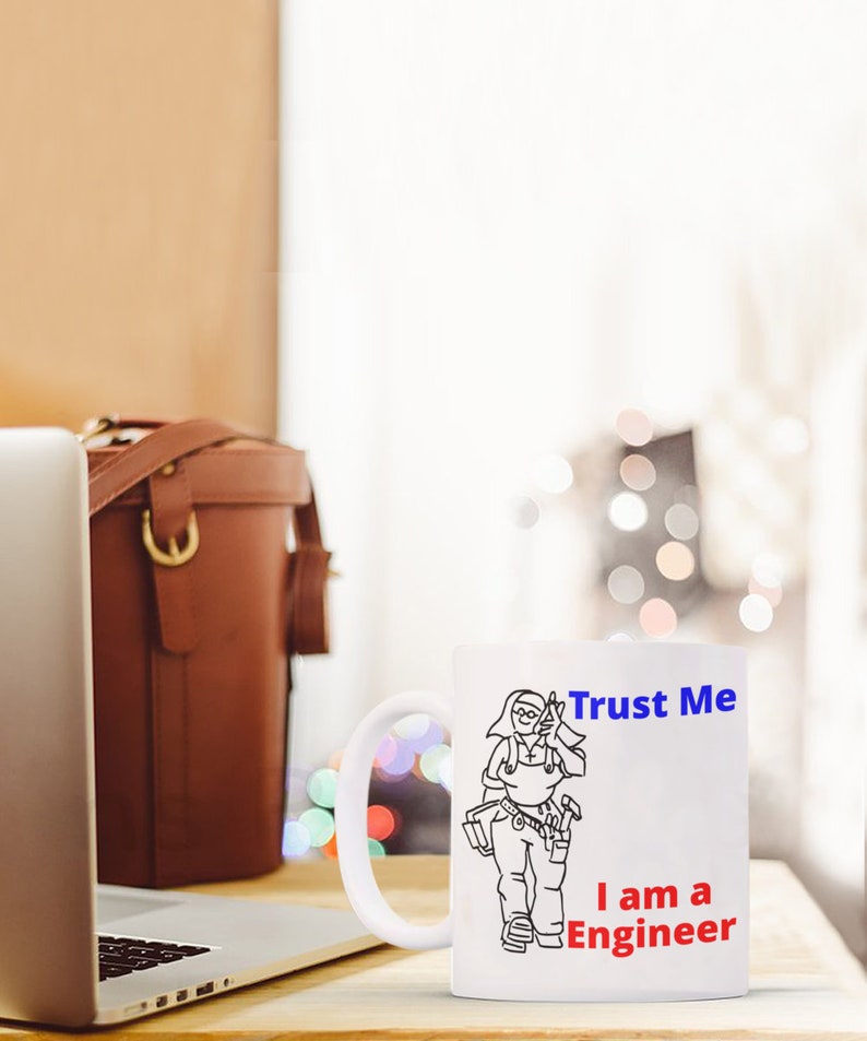 May include: White ceramic mug with a black line drawing of a person wearing a tool belt and holding a wrench. The text "Trust Me I am a Engineer" is printed on the mug in blue and red.