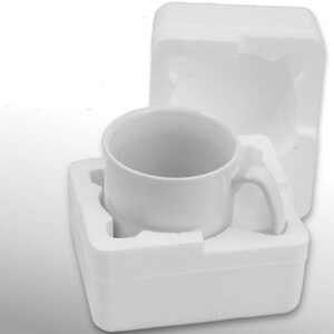 May include: A white ceramic mug with a handle, packaged in a white styrofoam box. The mug is sitting in a cutout in the box, with the handle sticking out.