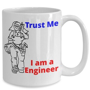 Könnte beinhalten: Eine weiße Keramiktasse mit einer Schwarzweißillustration einer Person mit Werkzeuggürtel und Hammer. Der Text "Trust Me I am a Engineer" ist in Blau und Rot auf die Tasse gedruckt.