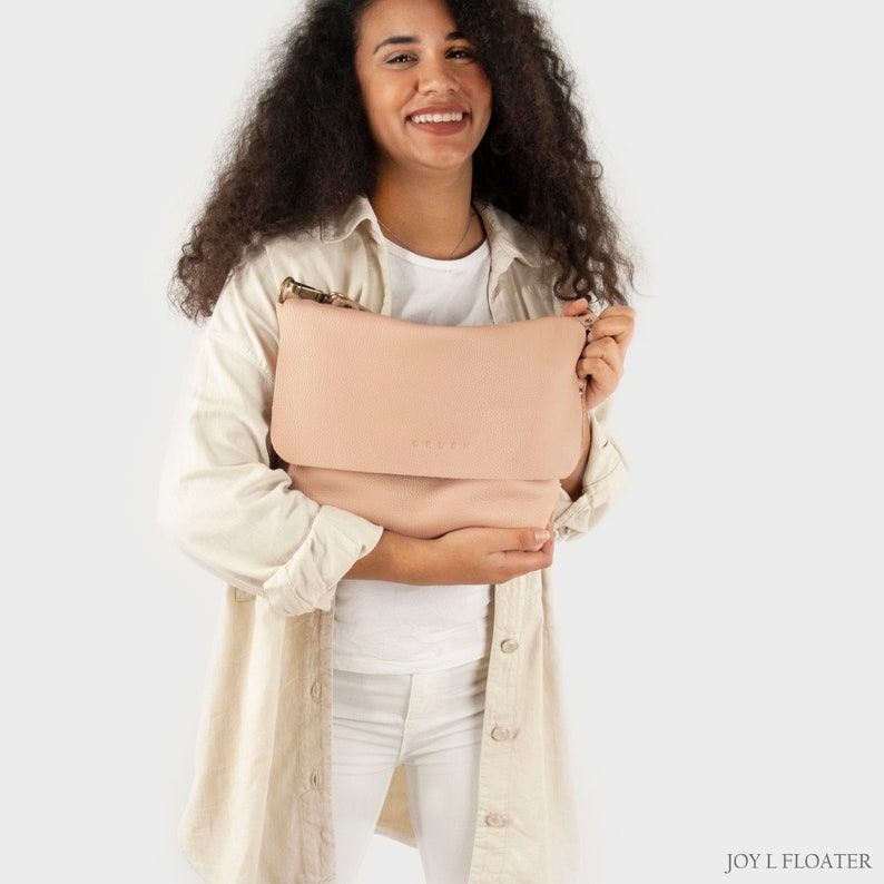 May include: A blush pink leather crossbody bag with a flap closure and a gold metal logo that reads 'COYLLI'.