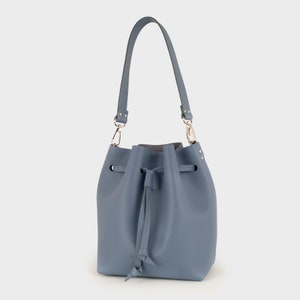May include: A light blue bucket bag with a drawstring closure and a silver chain strap. The bag has a small silver logo on the front.