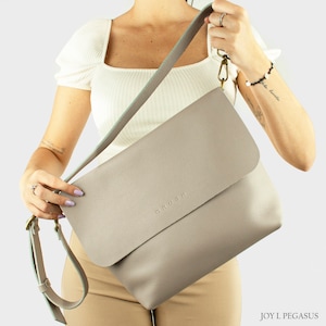 May include: A gray leather shoulder bag with a flap closure. The bag has a light blue strap and the word 'ORU.SH' embossed on the front.