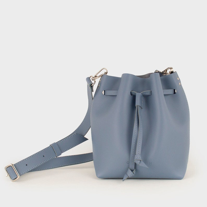 May include: A light blue leather bucket bag with a drawstring closure and a long adjustable strap.