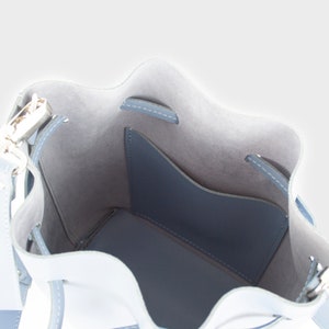 May include: The inside of a light blue bucket bag with a small pocket. The bag has a drawstring closure and a silver metal buckle.