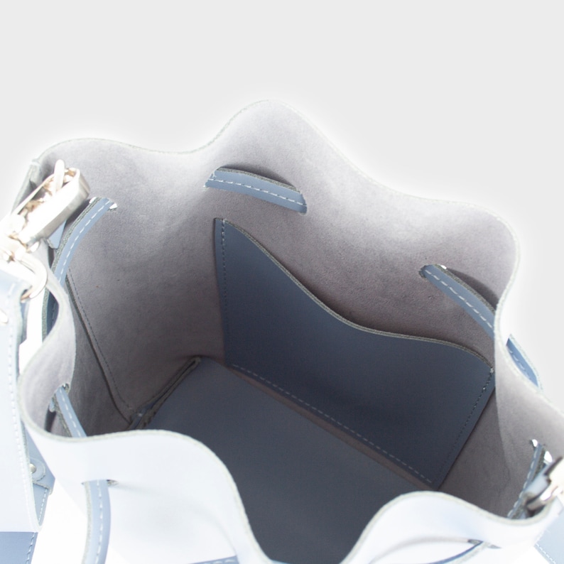 May include: The inside of a light blue bucket bag with a small pocket. The bag has a drawstring closure and a silver metal buckle.