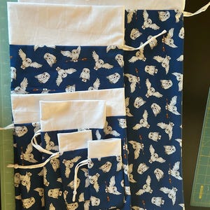 May include: Set of six drawstring bags in various sizes. The bags are made of white fabric with a blue owl print. The owls are white with black eyes and beaks. The bags are lined with white fabric.
