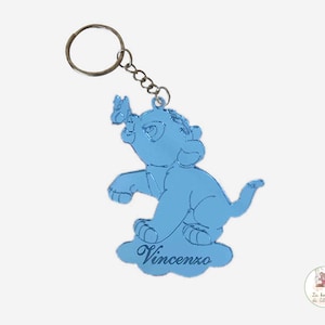 Op de afbeelding: Een lichtblauwe metalen sleutelhanger met een cartoon leeuwenwelp met een vlinder op zijn rug. De sleutelhanger heeft de naam "Vincenzo" gegraveerd op een wolk.
