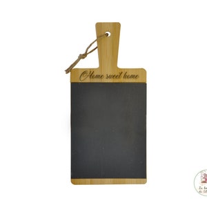 Op de afbeelding: Een houten snijplank met een oppervlak van schoolbord. De plank heeft een handvat en de tekst "Home sweet home" is bovenaan gegraveerd.
