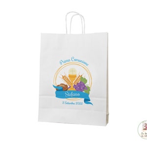 Può includere: Busta regalo di carta bianca con un nastro blu e un design circolare dorato. Il cerchio contiene un calice, pane, uva e grano. Il testo sulla busta recita "Prima Comunione Stefano 8 Settembre 2022".