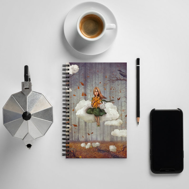 May include: A spiral bound notebook featuring a colourful illustration of a girl sitting on a cloud in a forest. The girl is holding a yellow flower and wearing a green dress. The background is a dark forest with falling leaves.
