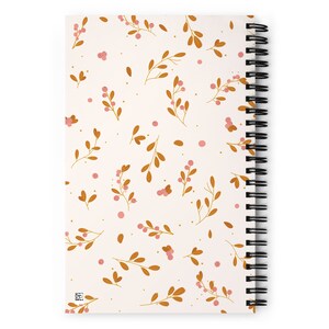 May include: A white spiral notebook with a floral pattern. The pattern features small pink berries and brown branches on a white background.