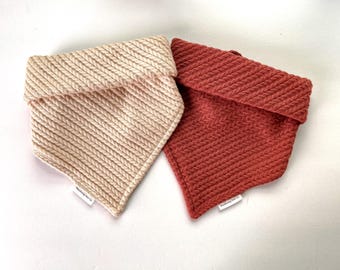 May include: Two knitted fabric dog bandanas, one in a light beige color and the other in a reddish-brown color. Both bandanas have a folded-over collar and a small white label with the text "Woodland Pet Co."