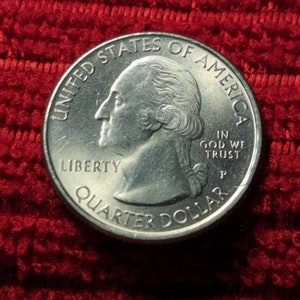 May include: A silver US quarter dollar coin with the image of George Washington on the obverse side. The coin has the words "United States of America", "Liberty", "In God We Trust", and "Quarter Dollar" inscribed on it.