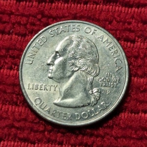 Peut inclure: Une pièce de monnaie américaine de 25 cents en argent avec les mots "United States of America" et "In God We Trust" sur le bord. La pièce représente un profil de George Washington et les mots "Liberty" et "Quarter Dollar".