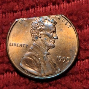 Puede incluir: Un centavo estadounidense de cobre de 1995 con las palabras "IN GOD WE TRUST" y "LIBERTY" en el anverso. La moneda presenta un perfil de Abraham Lincoln.