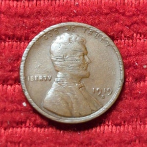 Puede incluir: Una moneda de un centavo estadounidense de cobre de 1919 con las palabras "LIBERTY" e "IN GOD WE TRUST" y el año "1919" inscrito en ella.