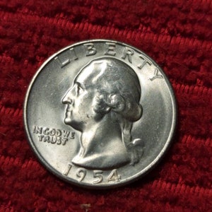 May include: A silver 1954 quarter coin, featuring a profile of George Washington and the inscriptions "LIBERTY" and "IN GOD WE TRUST." The coin is set against a red textured background.