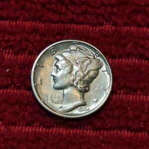 May include: A silver Mercury dime from 1944, featuring a profile of a woman wearing a winged Phrygian cap. The coin has the inscription "IN GOD WE TRUST" and is set against a red background.