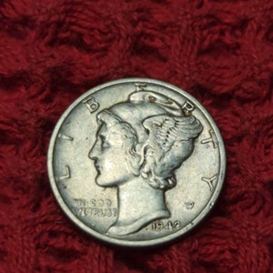 May include: A silver 1942 Mercury dime coin featuring the profile of a woman's head facing left. The coin has the words "In God We Trust" and "Liberty" inscribed on it.