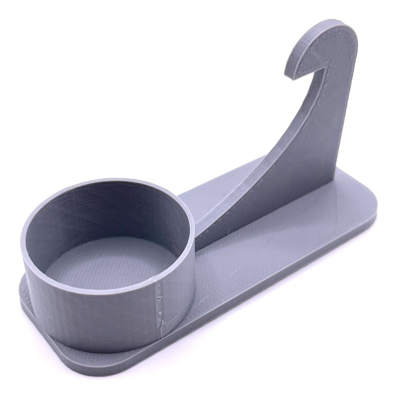 May include: A gray plastic phone stand with a circular base and a hook on the side. The stand is designed to hold a phone upright.