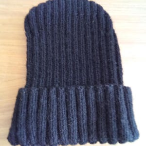 May include: A dark navy blue knitted beanie hat. The hat is made of a ribbed knit fabric. The brim is folded up, and the hat is a simple, classic design. The hat is likely made of wool or a wool blend.