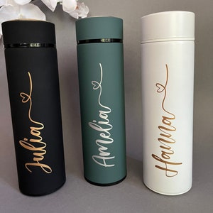 May include: Three personalized stainless steel water bottles with gold lettering. The bottles are black, green, and white. The names on the bottles are Julia, Amelia, and Hanna.