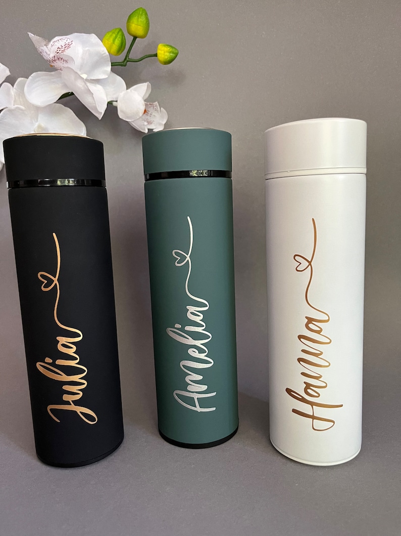 May include: Three personalized stainless steel water bottles with gold lettering. The bottles are black, green, and white. The names on the bottles are Julia, Amelia, and Hanna.