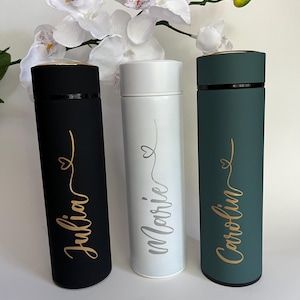 May include: Three personalized stainless steel water bottles with gold lettering. The bottles are black, white, and green. The names on the bottles are Julia, Marie, and Caroline.