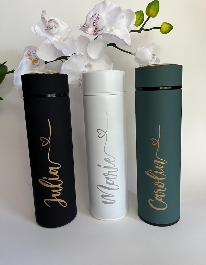 May include: Three personalized stainless steel water bottles with gold lettering. The bottles are black, white, and green. The names on the bottles are Julia, Marie, and Caroline.