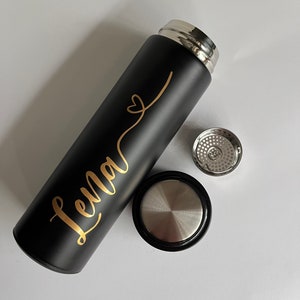 May include: Black stainless steel water bottle with a gold inscription that reads "Lena" with a heart symbol. The bottle has a black lid and a silver lid with a strainer.