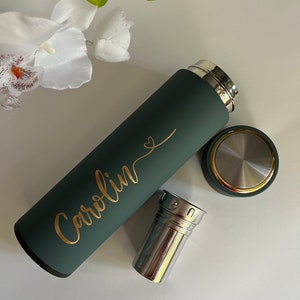 May include: A green reusable water bottle with a gold inscription that reads "Carolyn" with a heart symbol. The bottle has a stainless steel tea infuser.