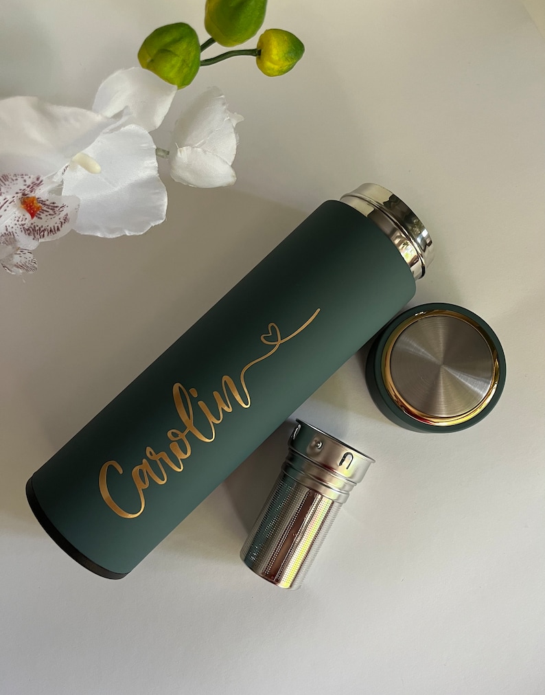 May include: A green reusable water bottle with a gold inscription that reads "Carolyn" with a heart symbol. The bottle has a stainless steel tea infuser.