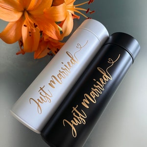 May include: Two stainless steel water bottles with the text "Just married" in gold lettering. One bottle is black and the other is white.