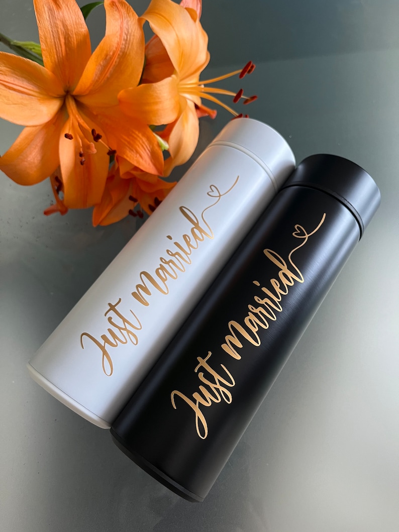 May include: Two stainless steel water bottles with the text "Just married" in gold lettering. One bottle is black and the other is white.