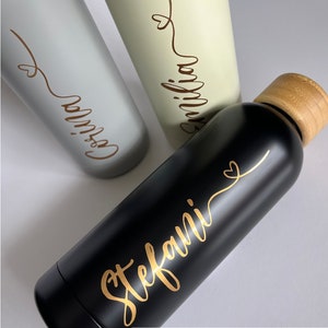 May include: Three stainless steel water bottles with bamboo lids. The bottles are personalized with gold lettering. The names on the bottles are "Emilia", "Gossia", and "Stefani".