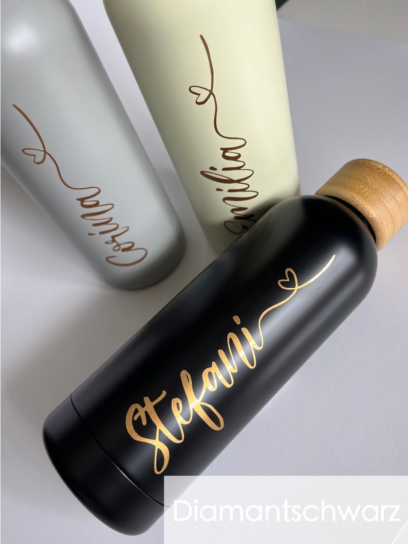 May include: Three stainless steel water bottles with bamboo lids. The bottles are personalized with gold lettering. The names on the bottles are "Emilia", "Gossia", and "Stefani".