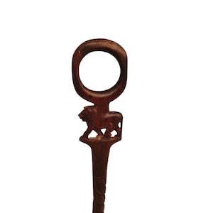 Puede incluir: Una cuchara de madera tallada de color marrón oscuro con una figura de león. La cuchara presenta un mango circular y un tallado detallado de un león en el tallo. La cuchara está sobre un fondo blanco.
