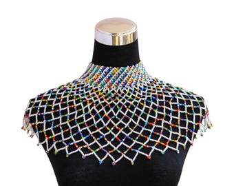 May include: A beaded collar necklace with a white net design and colorful beads. The necklace is displayed on a black mannequin, showcasing the intricate beadwork and vibrant colors.